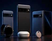 A lineup of phones with horizontal camera bars, a foldable phone, round smartwatch, an earbuds case and an item tracker on a dark background.