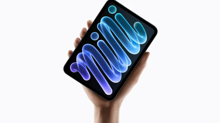 Apple iPad mini held in one hand, with a blue and violet pattern on its screen