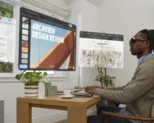 Man wearing XREAL AURA at a desk, surrounded by illustrated virtual app windows